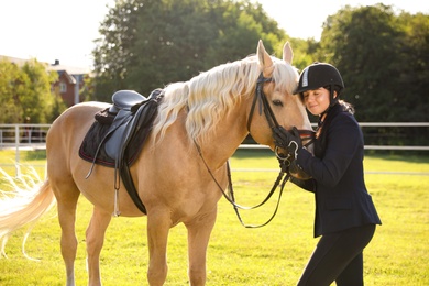 Photo of Young woman in horse riding suit and her beautiful pet outdoors on sunny day