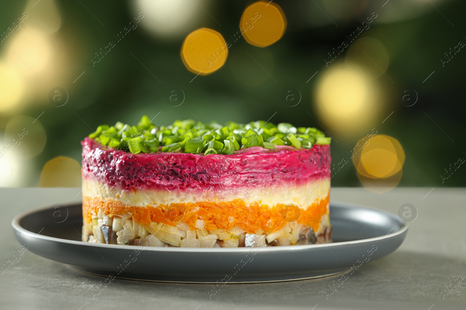 Photo of Herring under fur coat salad on grey table against blurred festive lights, closeup with space for text. Traditional Russian dish