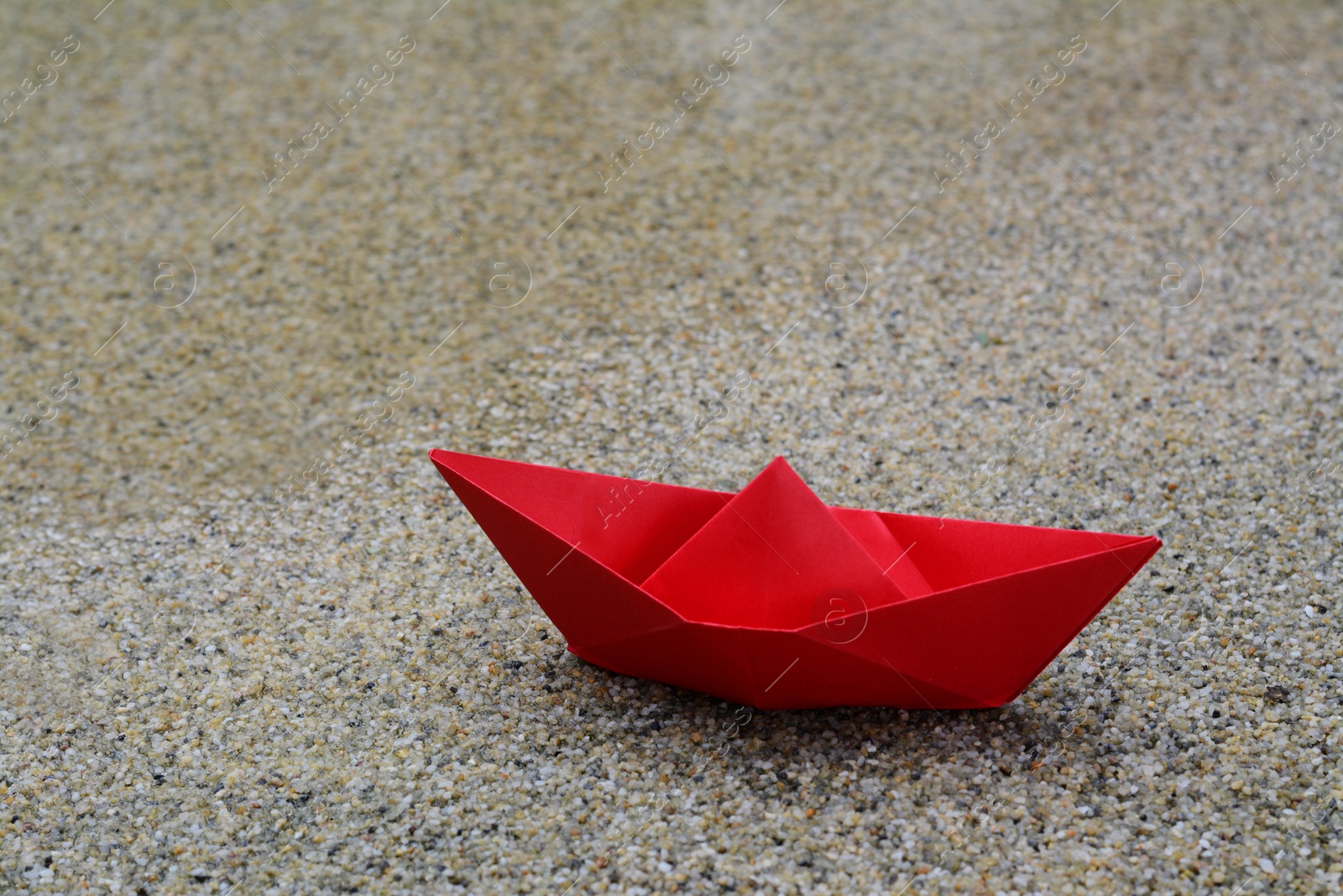 Photo of Beautiful red paper boat on sandy beach near water outdoors