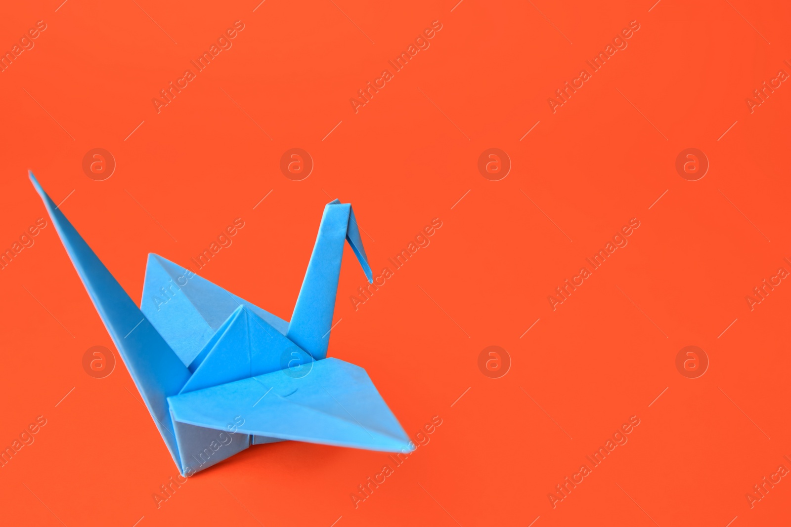 Photo of Origami art. Handmade paper crane on orange background, space for text