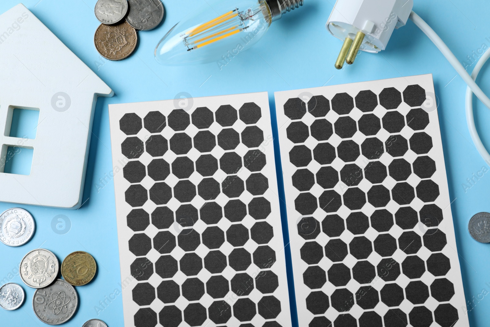 Photo of Flat lay composition with solar panels, house model, light bulb and and coins on light blue background