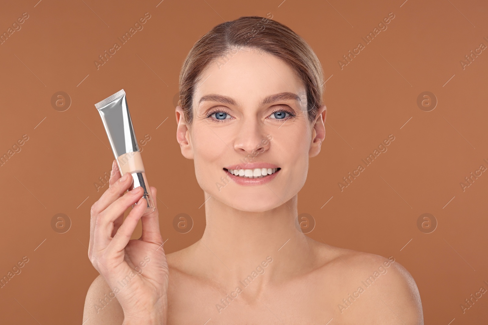 Photo of Woman holding tube of foundation on brown background