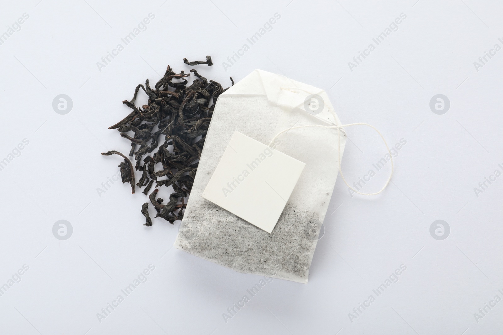 Photo of Dry tea leaves and unused bag with tag on white background, top view. Space for text