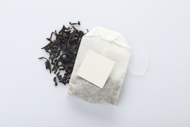 Photo of Dry tea leaves and unused bag with tag on white background, top view. Space for text