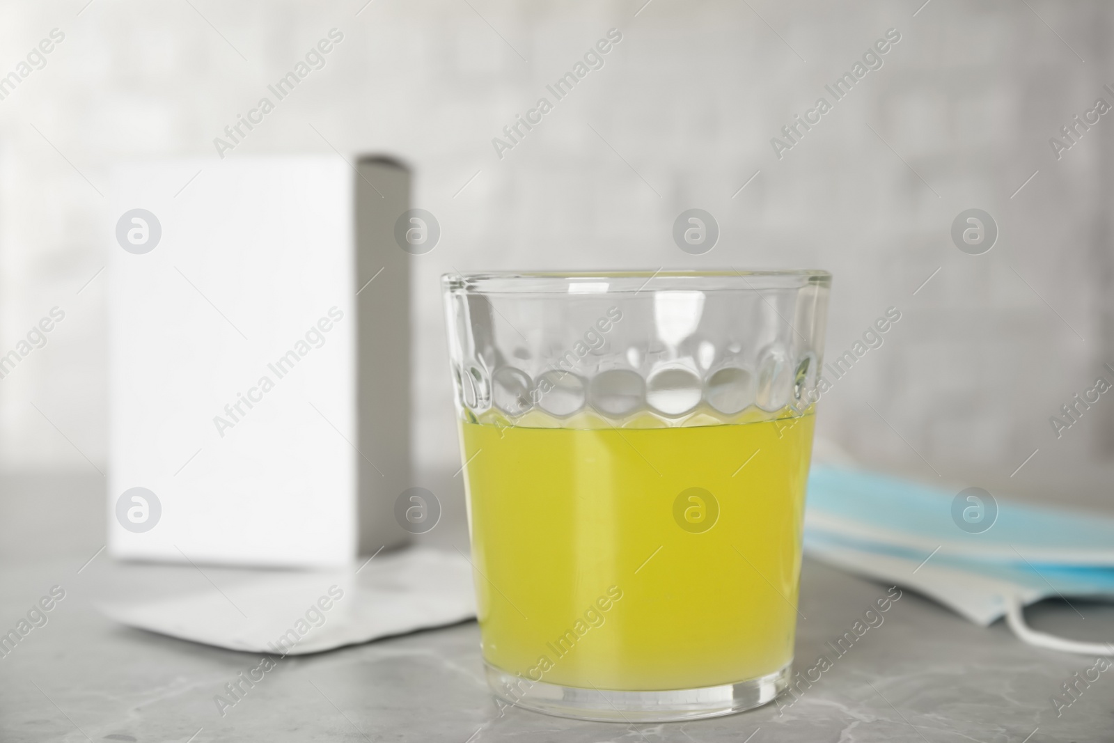 Photo of Glass of dissolved medicine and sachet on grey marble table, closeup