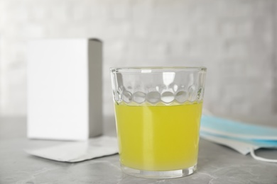 Glass of dissolved medicine and sachet on grey marble table, closeup