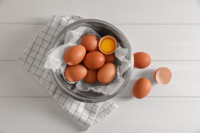 Fresh raw chicken eggs with bowl and napkin on white wooden table, flat lay