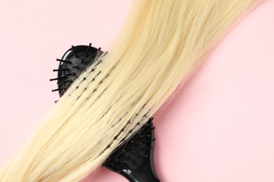 Photo of Stylish brush with blonde hair strand on pink background, top view