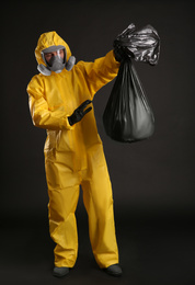 Man in chemical protective suit holding trash bag on black background. Virus research