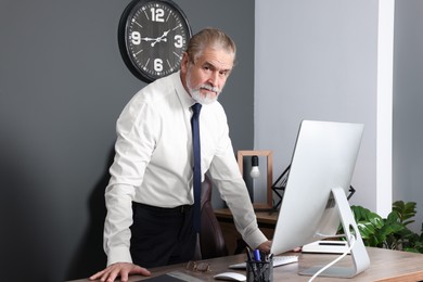 Photo of Serious senior boss near wooden table with computer in office