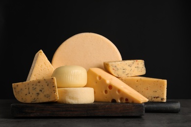Photo of Wooden board with different sorts of cheese on table against black background