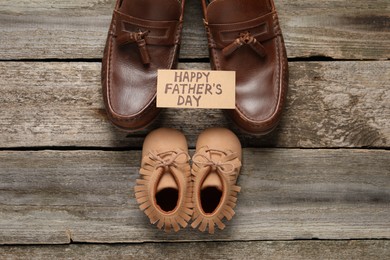Photo of HAPPY FATHER'S DAY. Dad and son's shoes on wooden background, flat lay