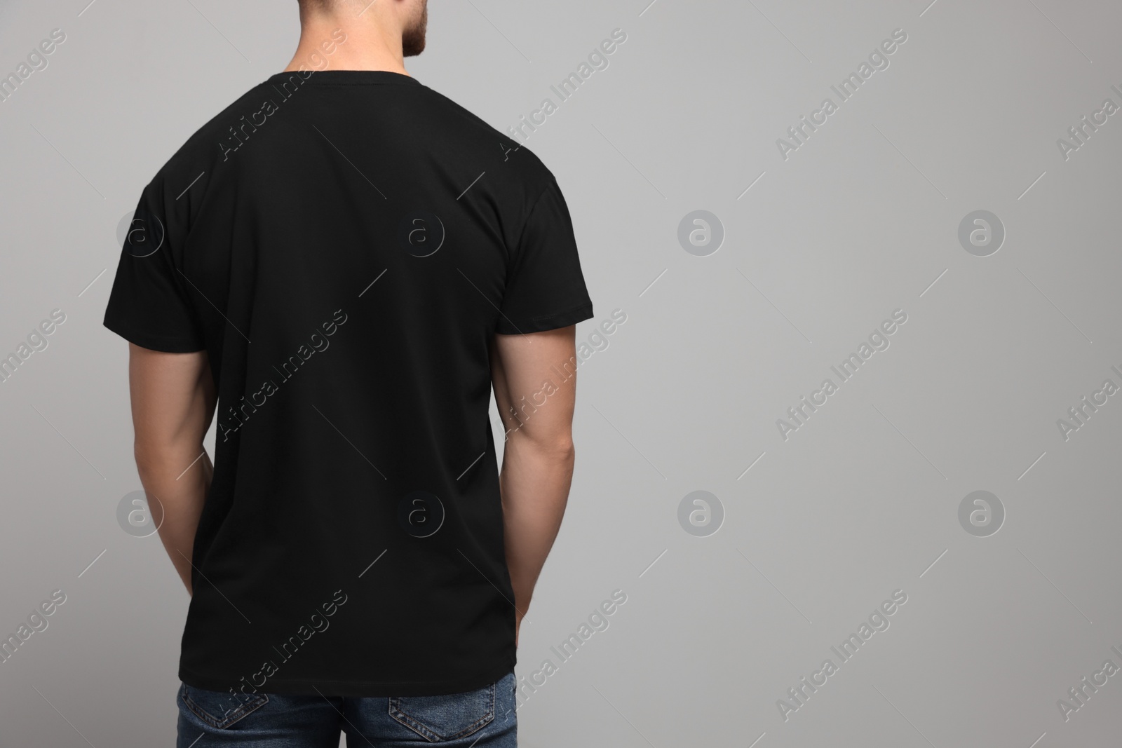 Photo of Man wearing black t-shirt on light grey background, back view. Mockup for design