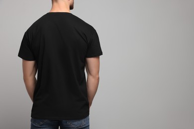 Man wearing black t-shirt on light grey background, back view. Mockup for design