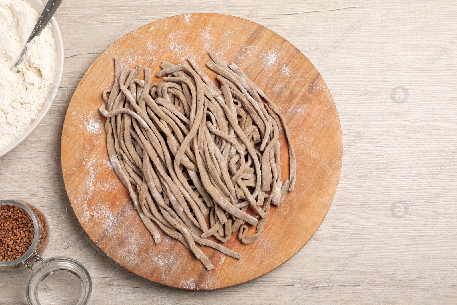 Photo of Uncooked homemade soba (buckwheat noodles), flour and grains on wooden table, flat lay