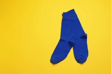 Photo of Blue socks on yellow background, flat lay. Space for text
