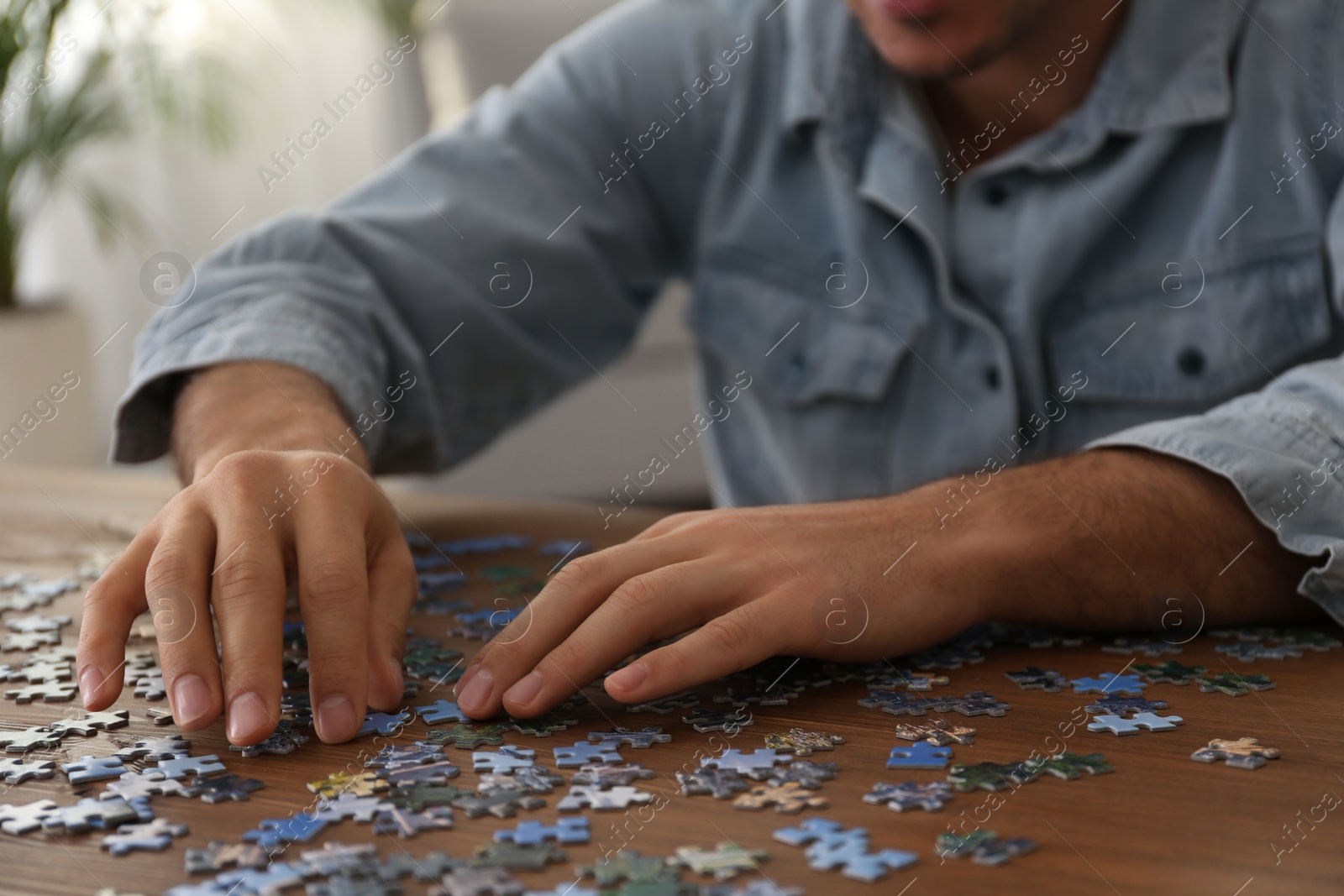 Photo of Man playing with puzzles at wooden table indoors, closeup