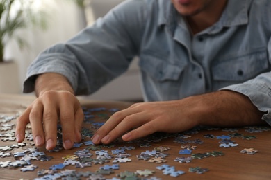 Man playing with puzzles at wooden table indoors, closeup