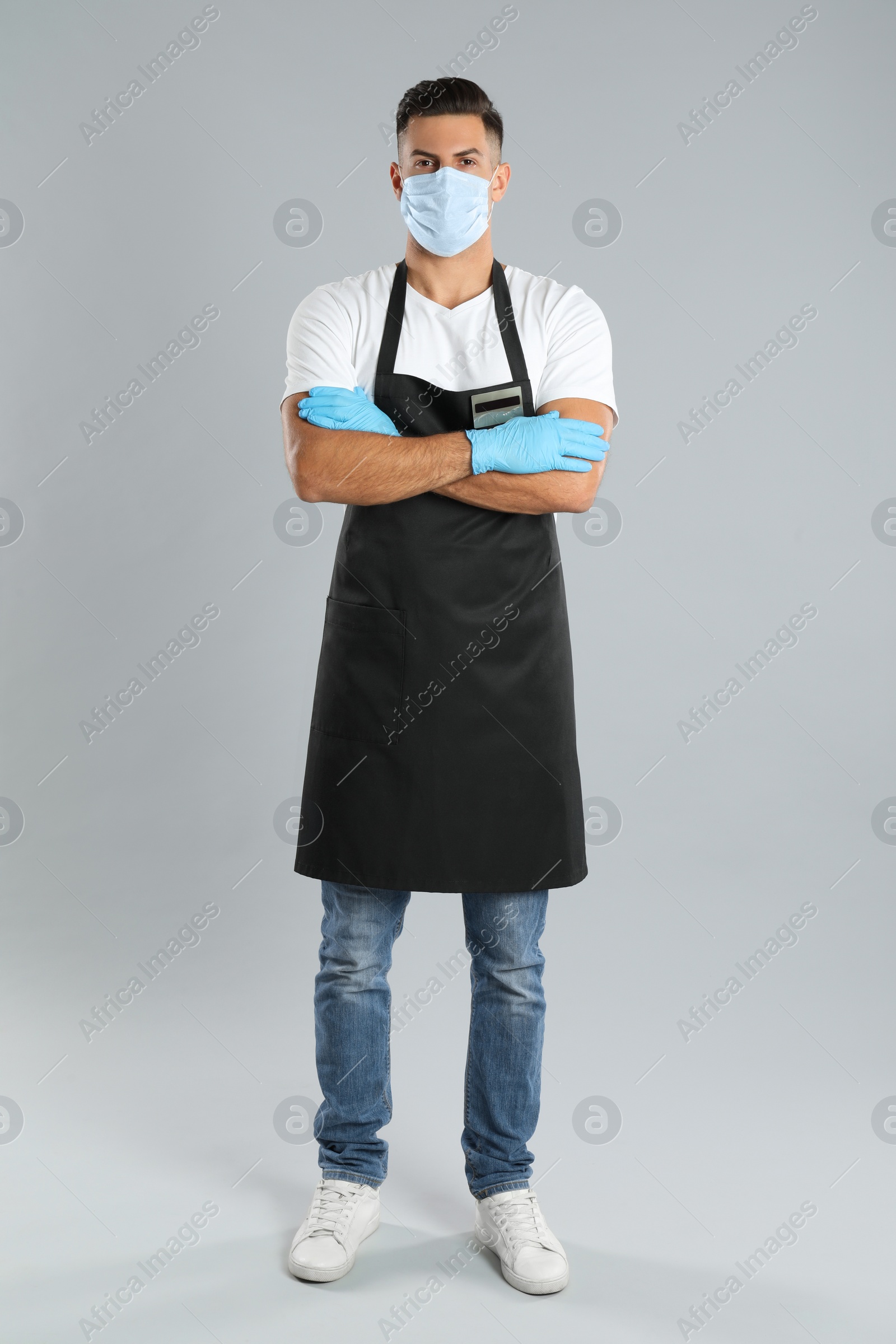 Photo of Waiter wearing medical face mask on light grey background