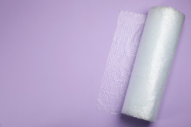 Photo of Bubble wrap roll on lilac background, top view. Space for text