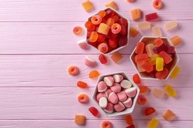 Photo of Flat lay composition with bowls of tasty jelly candies on pink wooden table, space for text