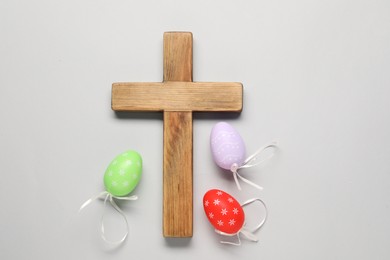 Wooden cross and painted Easter eggs on light grey background, flat lay