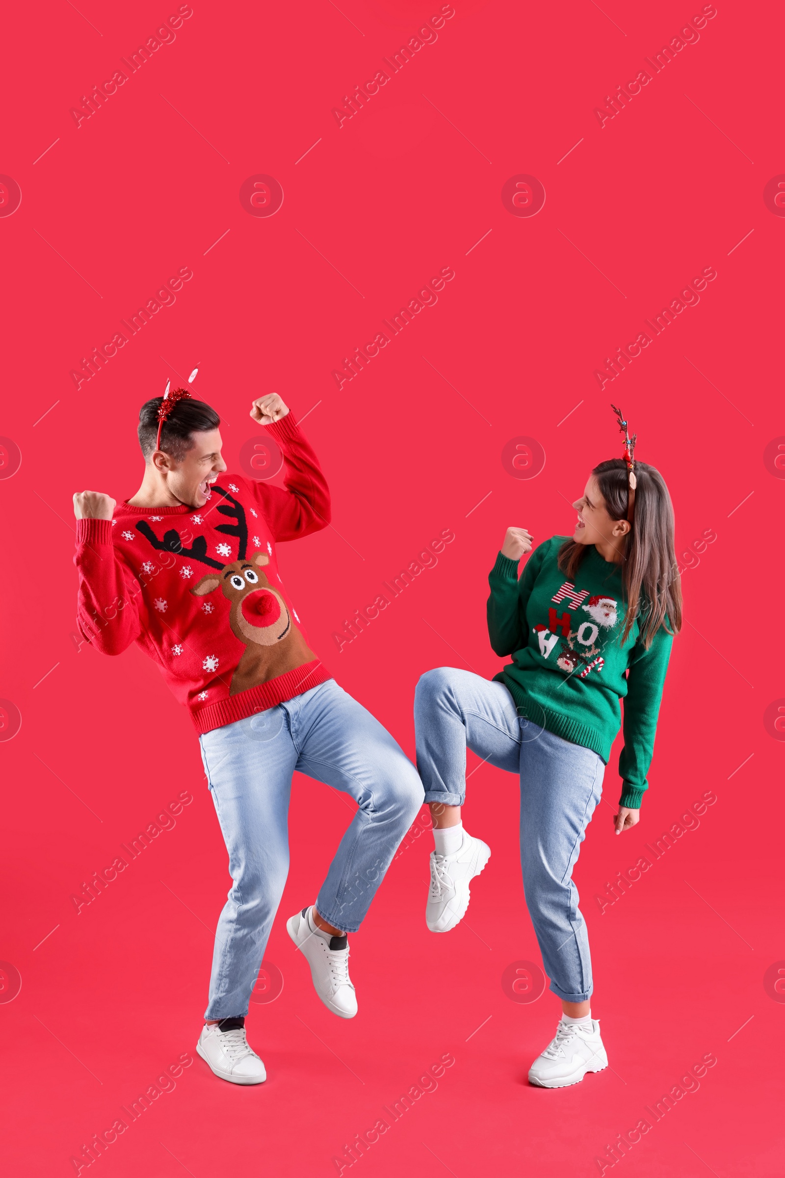 Photo of Beautiful happy couple in Santa hats and Christmas sweaters having fun on red background