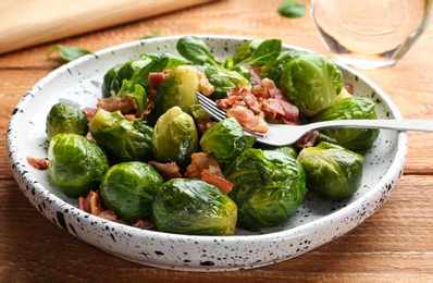 Photo of Tasty roasted Brussels sprouts with bacon on wooden table, closeup