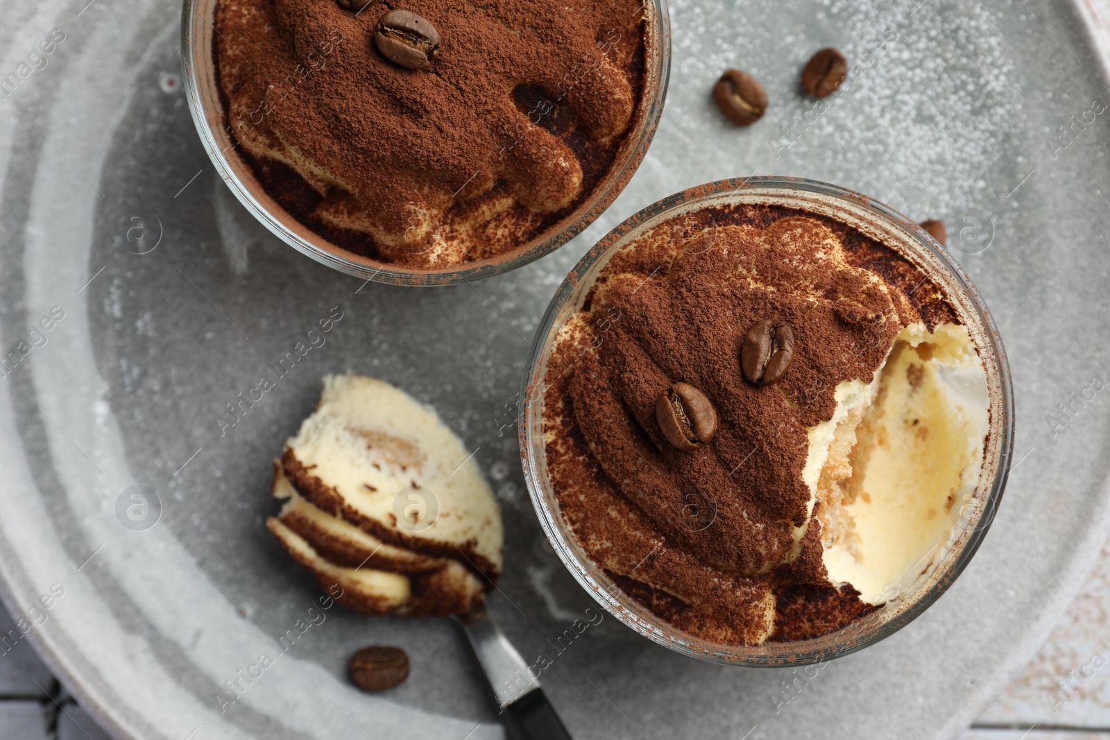 Photo of Delicious tiramisu in glasses, spoon and coffee beans on table, top view