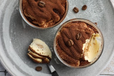 Photo of Delicious tiramisu in glasses, spoon and coffee beans on table, top view