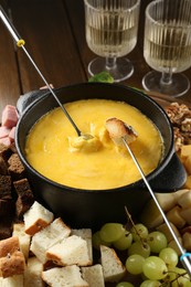 Photo of Fondue pot with melted cheese, glasses of wine and different products on wooden table