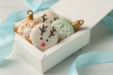 Photo of Beautifully decorated Christmas macarons in box and ribbon on white table, closeup