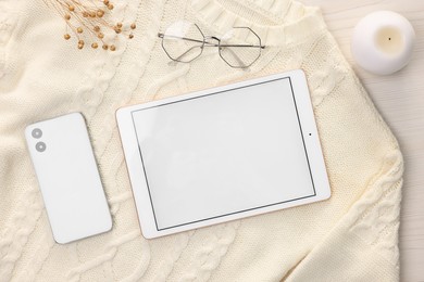 Photo of Modern tablet, glasses, smartphone, candle and sweater on white wooden table, flat lay. Space for text