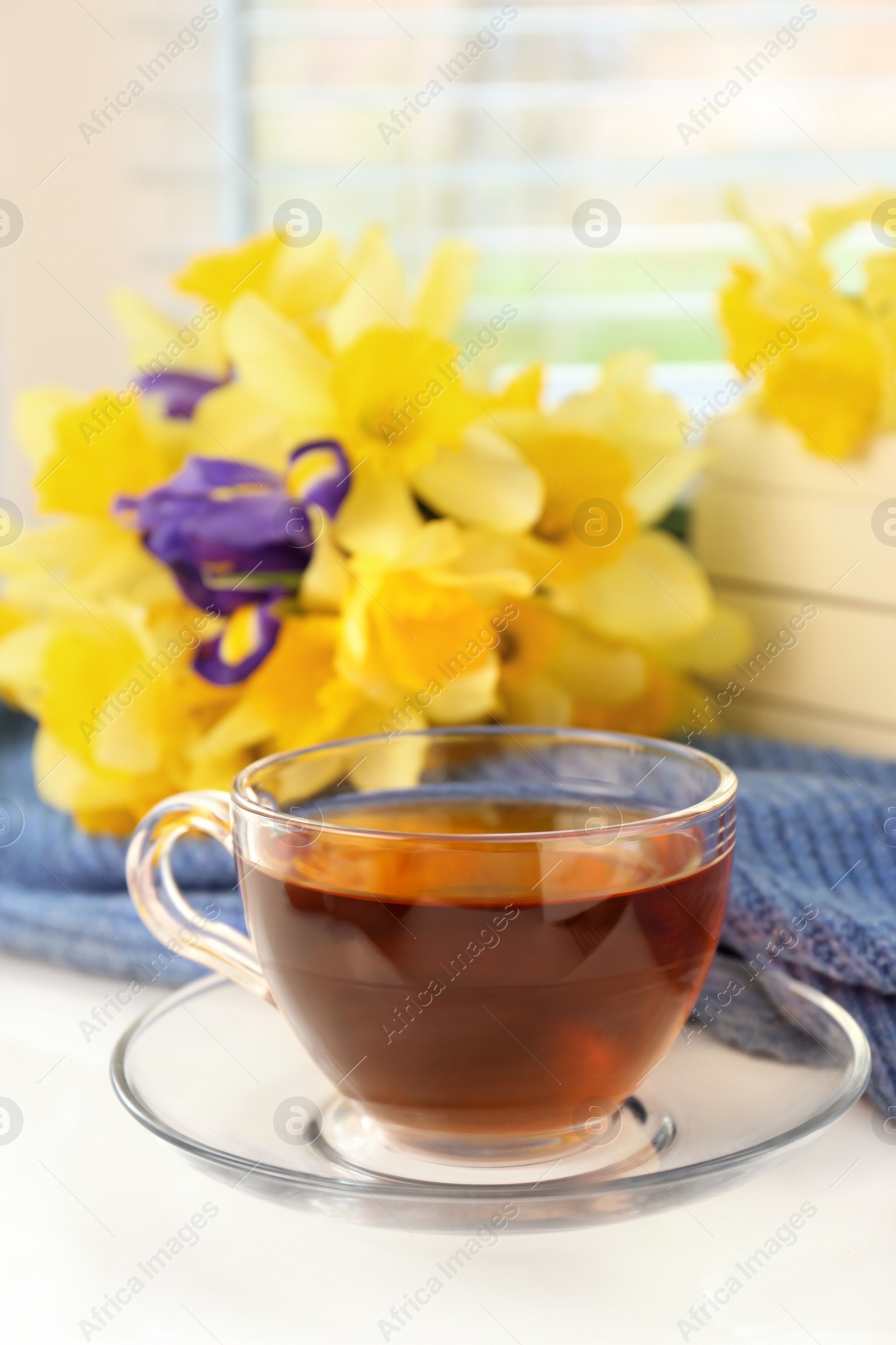 Photo of Cup of aromatic tea, beautiful yellow daffodil and iris flowers on windowsill. Space for text