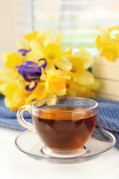 Cup of aromatic tea, beautiful yellow daffodil and iris flowers on windowsill. Space for text