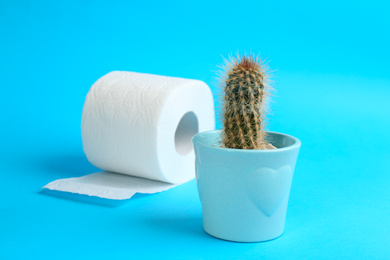 Photo of Roll of toilet paper and cactus on light blue background. Hemorrhoid problems