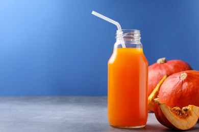 Photo of Tasty pumpkin juice in glass bottle and pumpkins on light grey table against blue background. Space for text
