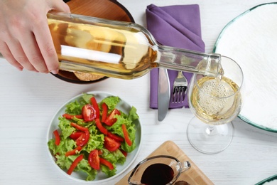 Woman pouring white wine into glass on table with delicious food, closeup