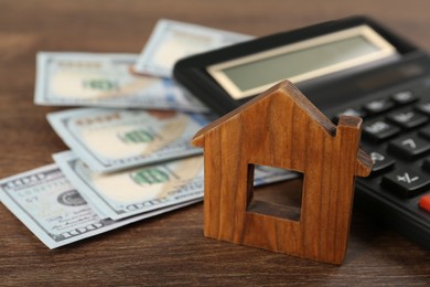 Photo of Mortgage concept. House model, calculator and money on wooden table, closeup