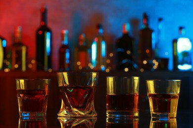 Photo of Different liqueurs in glasses on mirror table in bar, closeup