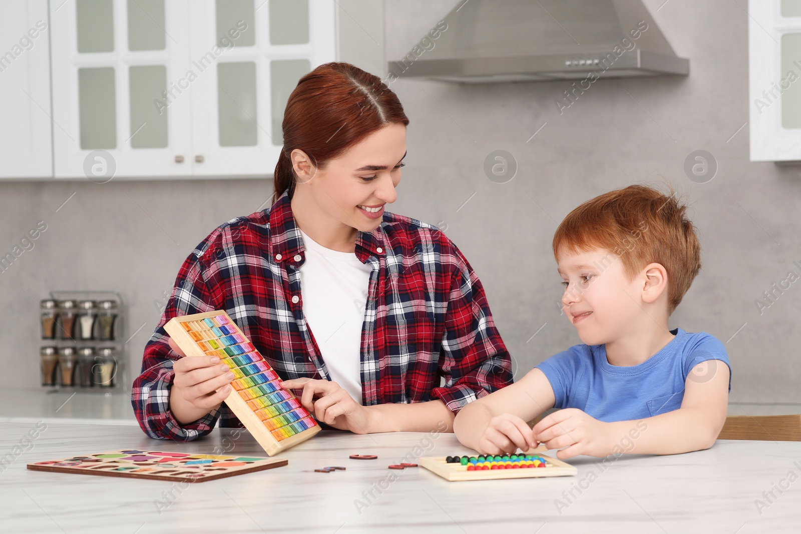 Photo of Happy mother and son playing with different colorful cubes and equations at white marble table in kitchen. Learning mathematics with fun