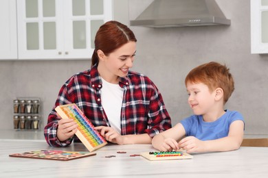 Happy mother and son playing with different colorful cubes and equations at white marble table in kitchen. Learning mathematics with fun