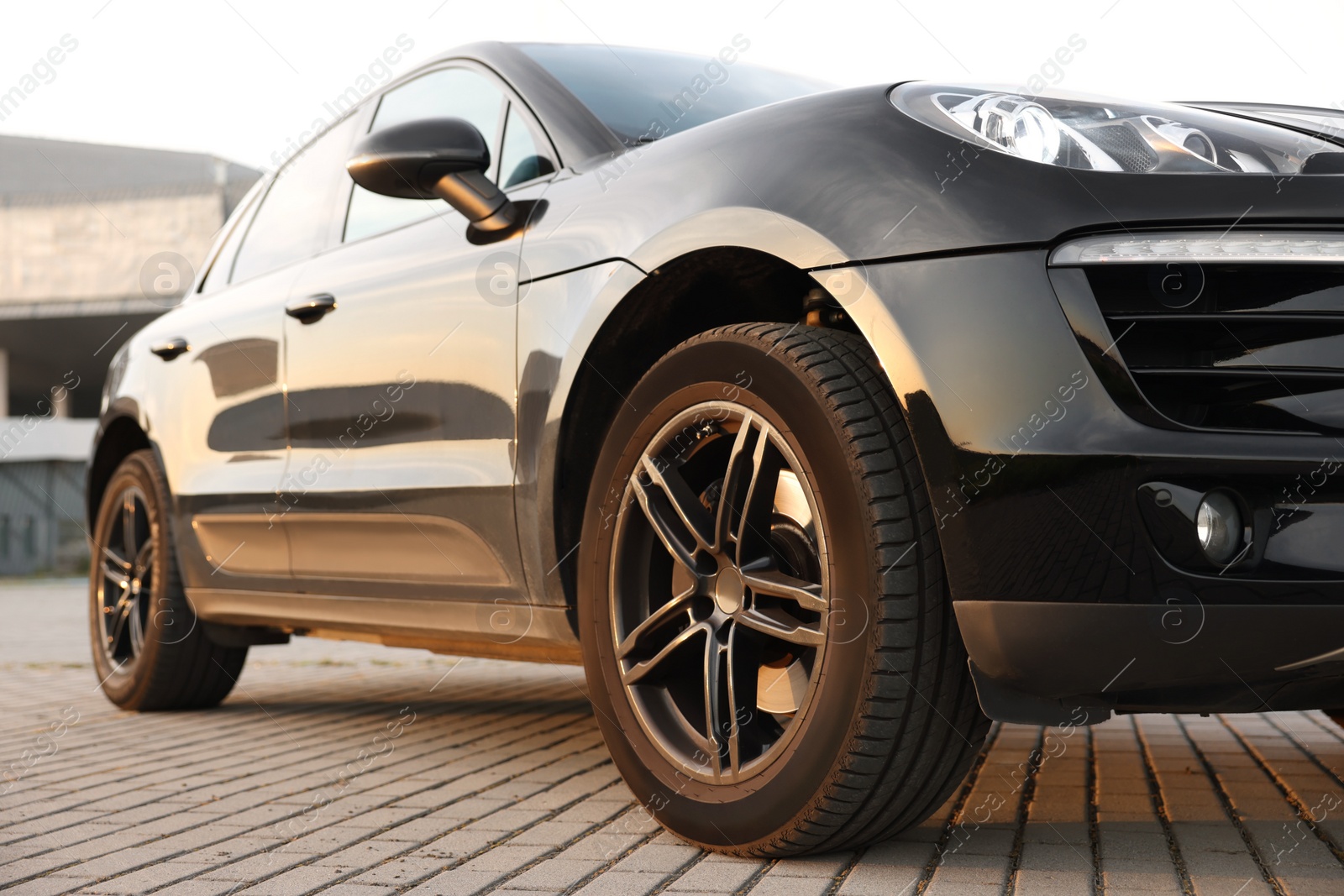 Photo of Modern black car parked on stone pavement outdoors