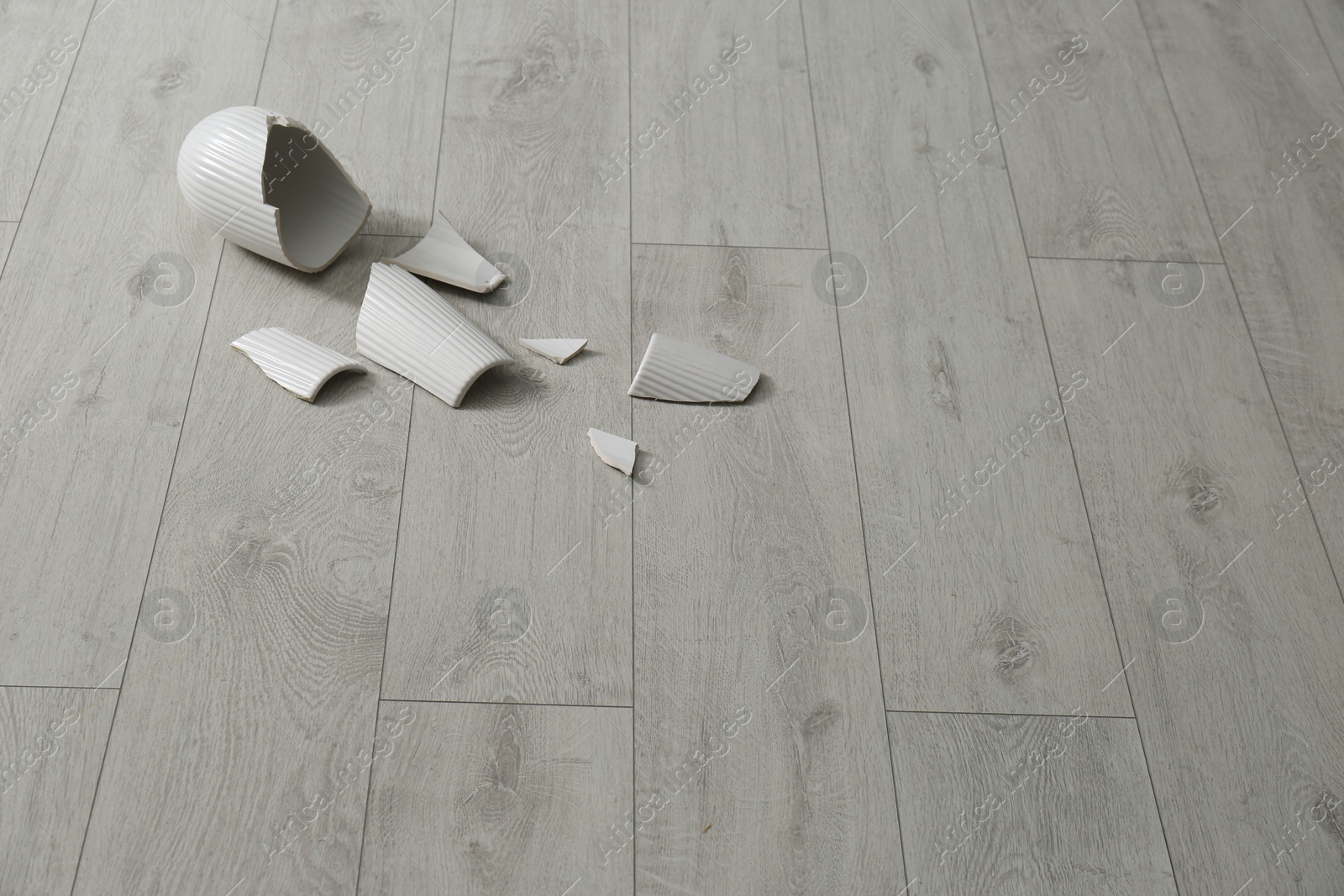 Photo of Broken ceramic vase on wooden floor. Space for text