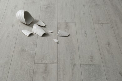 Broken ceramic vase on wooden floor. Space for text