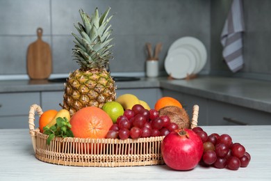 Photo of Wicker tray and different ripe fruits on white wooden table in kitchen