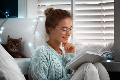Photo of Young woman reading book at home. Cozy winter
