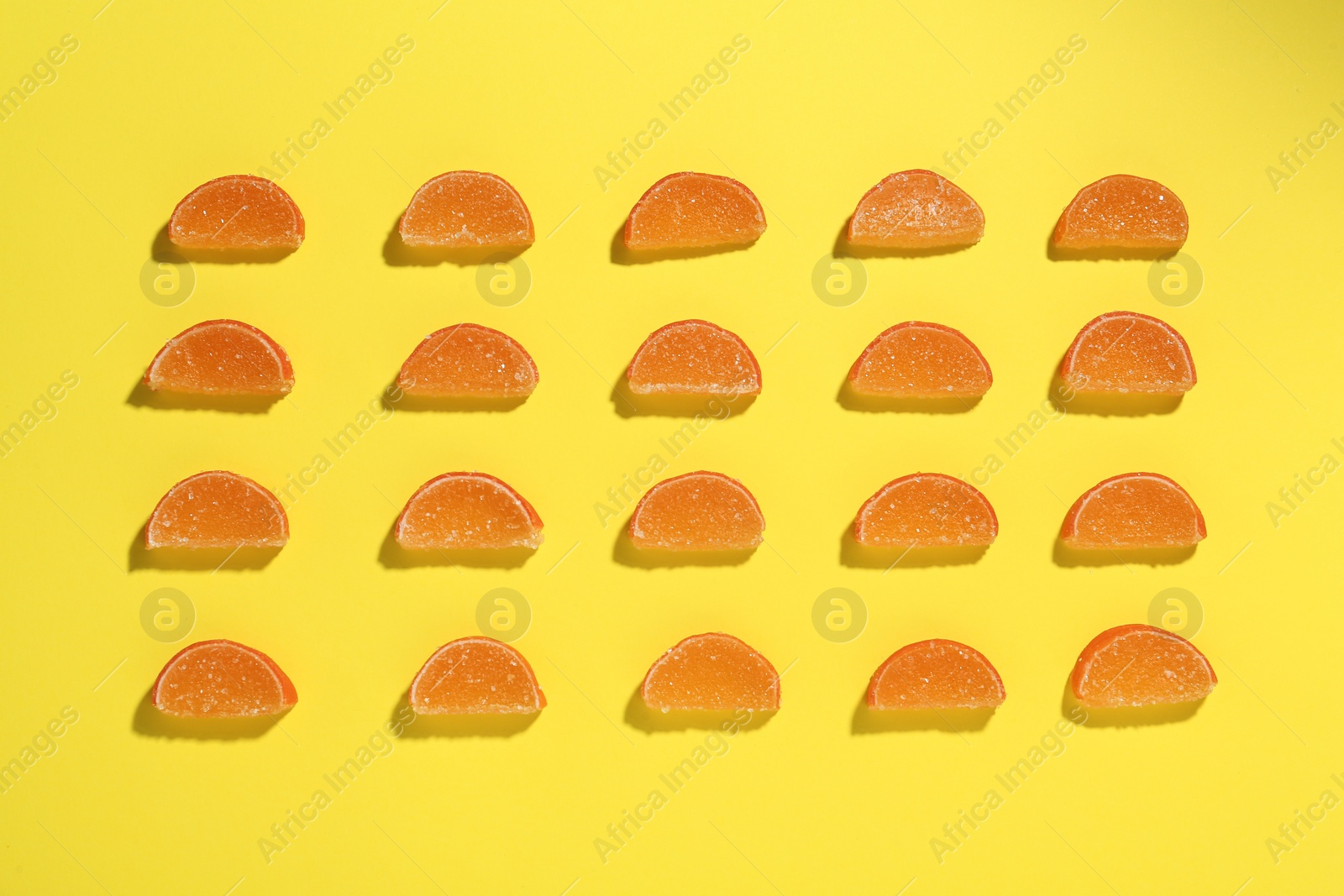 Photo of Delicious orange marmalade candies on yellow background, flat lay