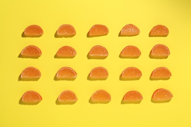 Photo of Delicious orange marmalade candies on yellow background, flat lay