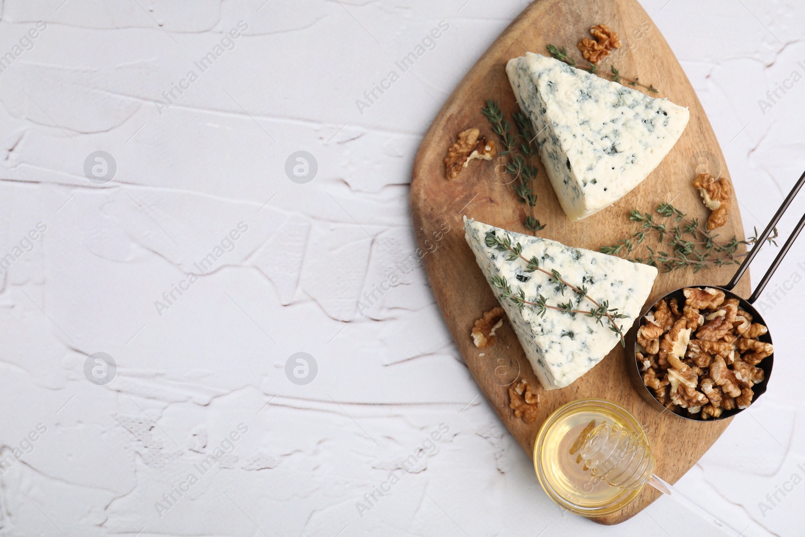 Photo of Tasty blue cheese with thyme, honey and walnuts on white textured table, top view. Space for text